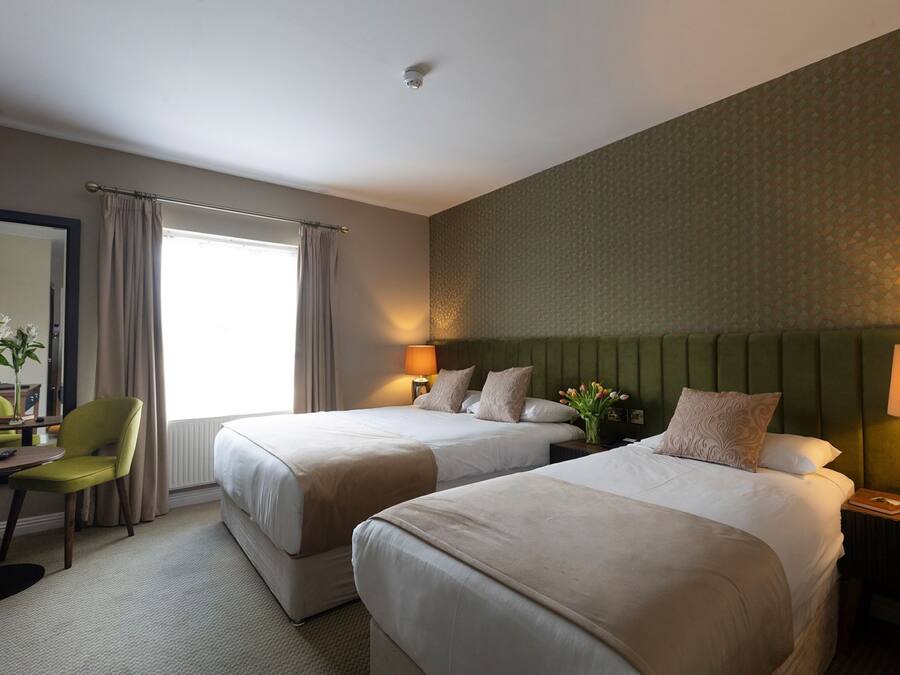 A hotel room with two beds, a desk with a chair, a mirror, and a window with curtains.
