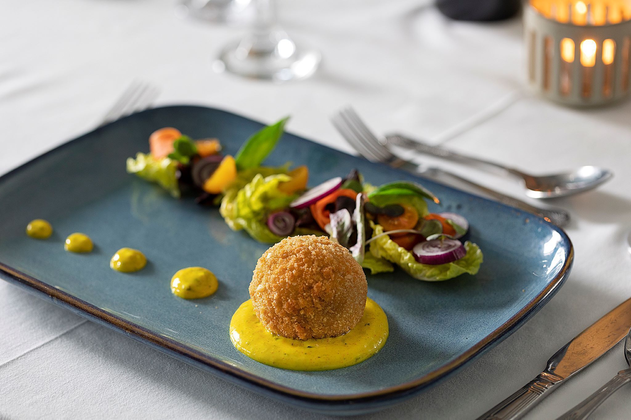 A plated dish with a spherical item, a salad, and yellow sauce on a blue plate.