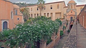 A narrow alleyway with buildings on either side, featuring a small garden with white flowers and a palm tree. - Atlantica Yakinthos Hotel (Chania)