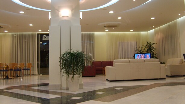 A modern lobby with a central column, seating area, and a television screen. - Atlantica Yakinthos Hotel (Chania)