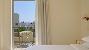 A hotel room with a balcony, a bed, a table, and a lamp. - Atlantica Yakinthos Hotel (Chania)