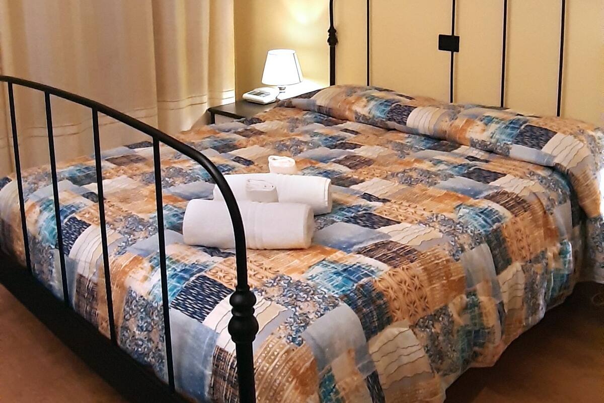 A bed with a quilt, a nightstand with a lamp, and a painting on the wall.
