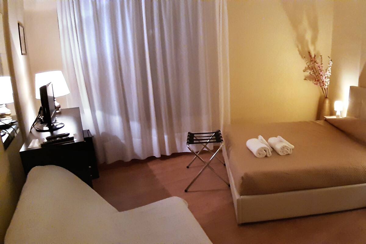A hotel room with a bed, a desk with a lamp, a chair, and a nightstand with a lamp.