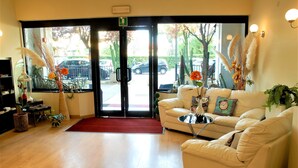 A hotel lobby with a sofa, a small table, a red carpet, and a view of the street through the glass doors. - Hotel Provenza (Ventimiglia)