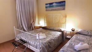A bedroom with two beds, a nightstand, a lamp, a painting of a beach, and a window with curtains. - Hotel Provenza (Ventimiglia)