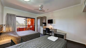A hotel room with two beds, a desk, a chair, a television, and a ceiling fan.