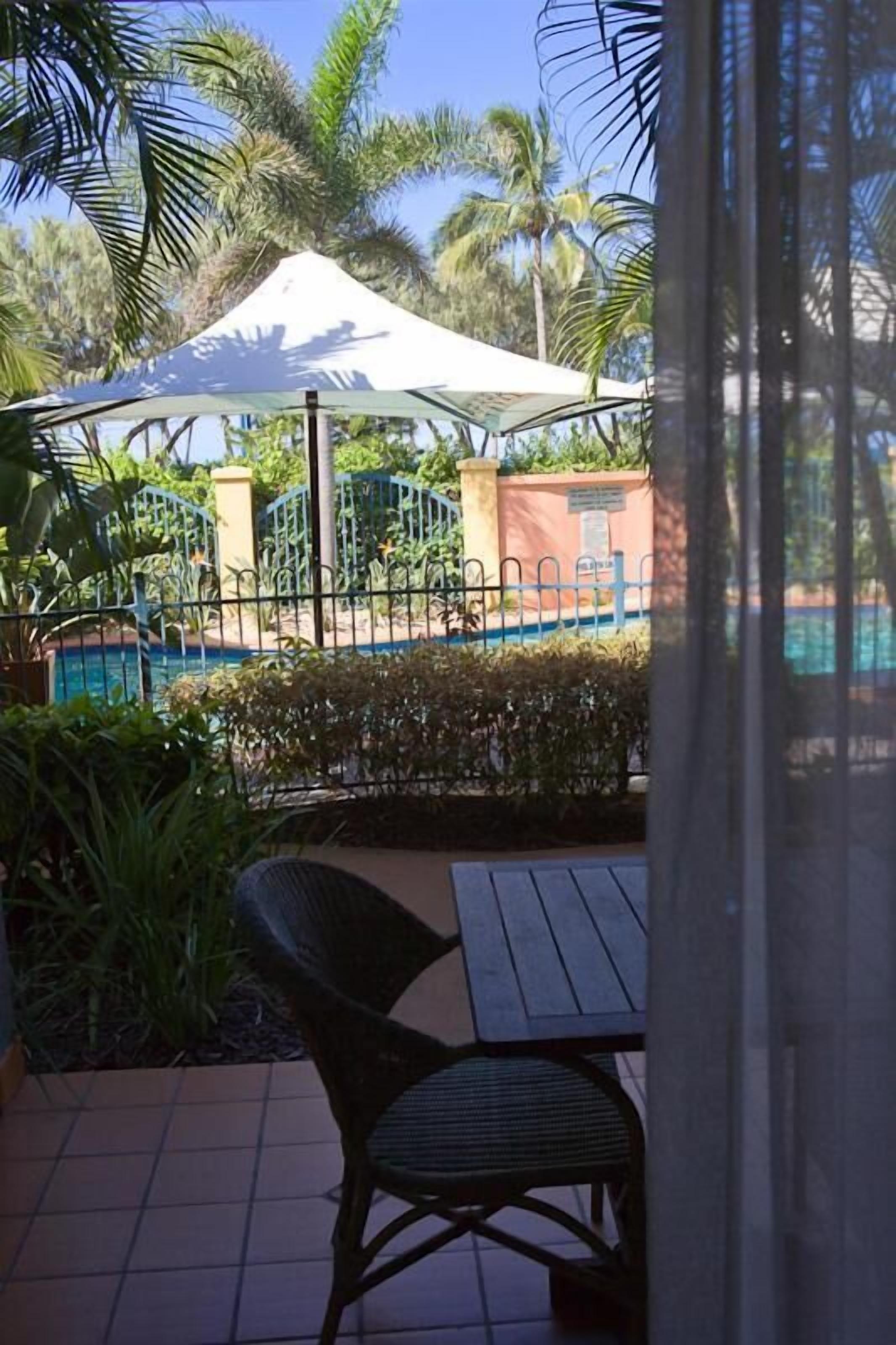 Un patio con mesa y sillas, una piscina y una carpa blanca al fondo.