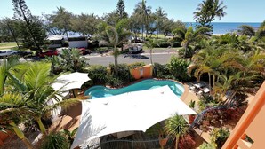 Zona de piscina con vista al océano, rodeada de palmeras y un deck cercado.