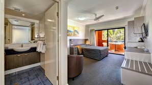 Habitación de hotel con baño, cama, escritorio y balcón con vistas.