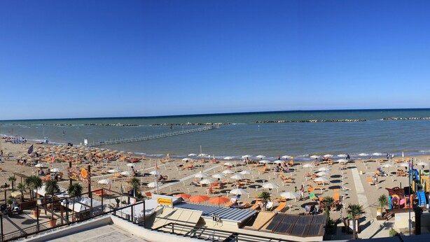 A beach with numerous umbrellas and sun loungers, a pier extending into the sea, and a clear blue sky. - Strand (Bellaria-Igea Marina)