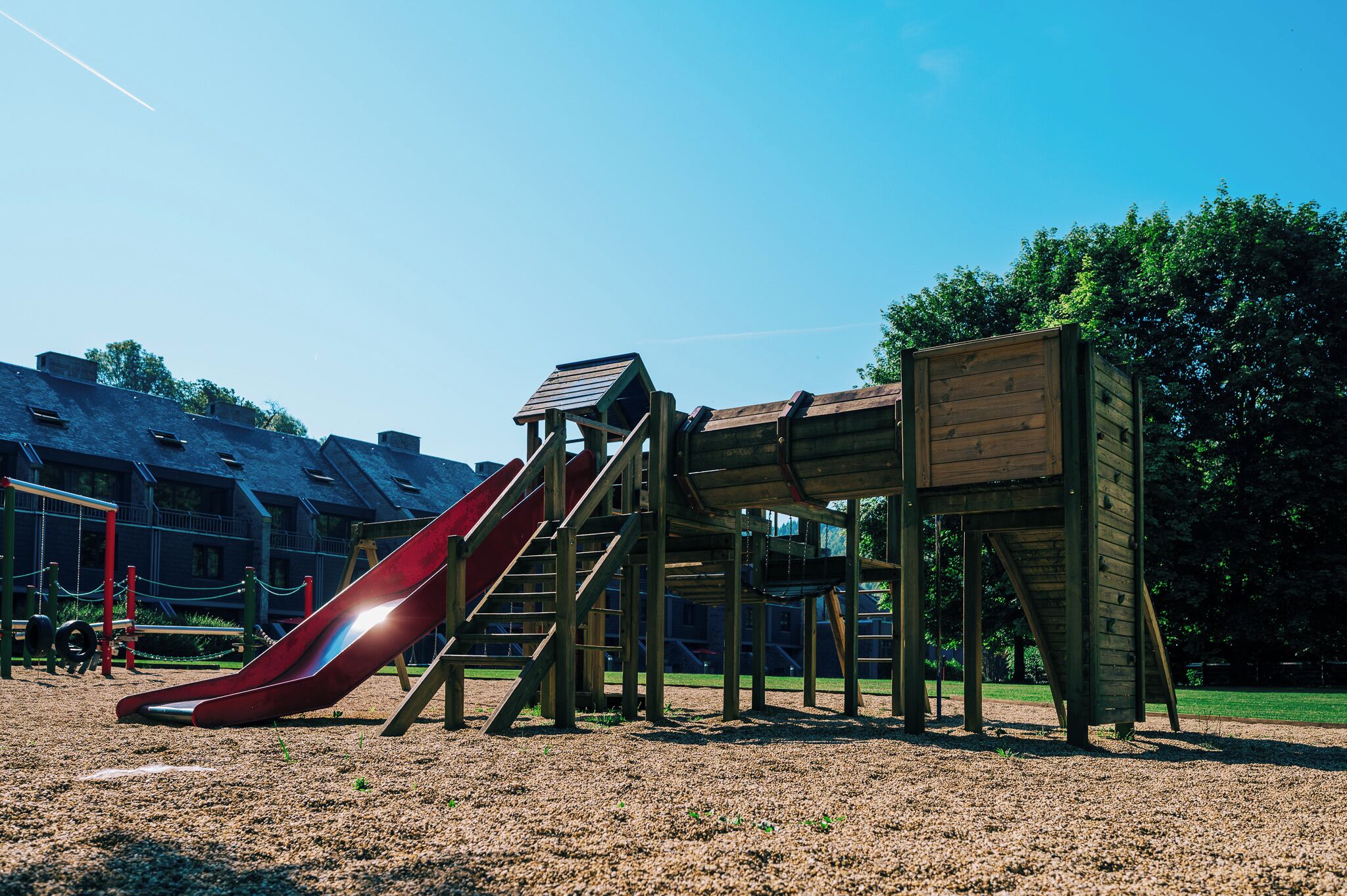Un parque infantil con un tobogán rojo y estructuras de madera para escalar.