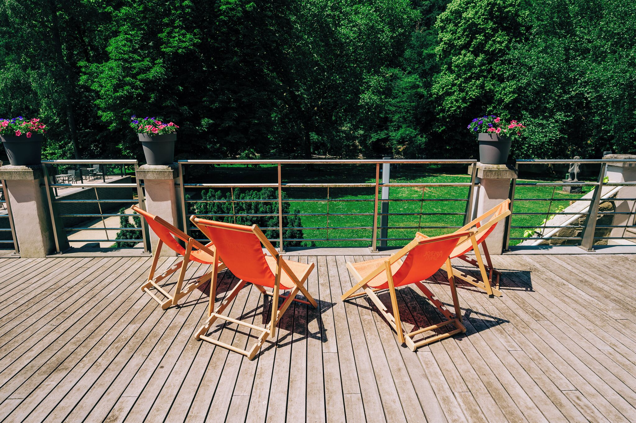 Une terrasse en bois avec deux chaises orange et des plantes en pot.