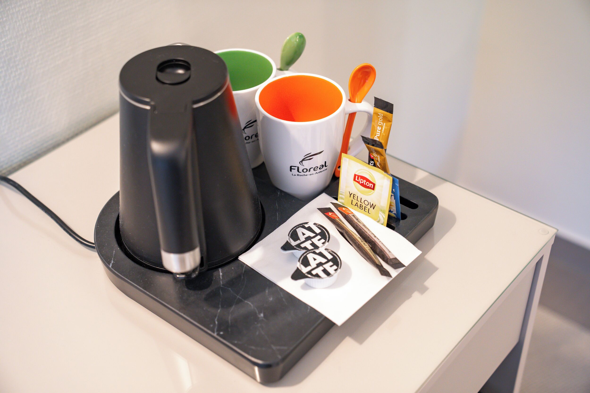 A coffee maker, two mugs, a spoon, and a Lipton tea packet on a counter.