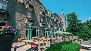 A stone building with a tower, outdoor seating, and umbrellas.