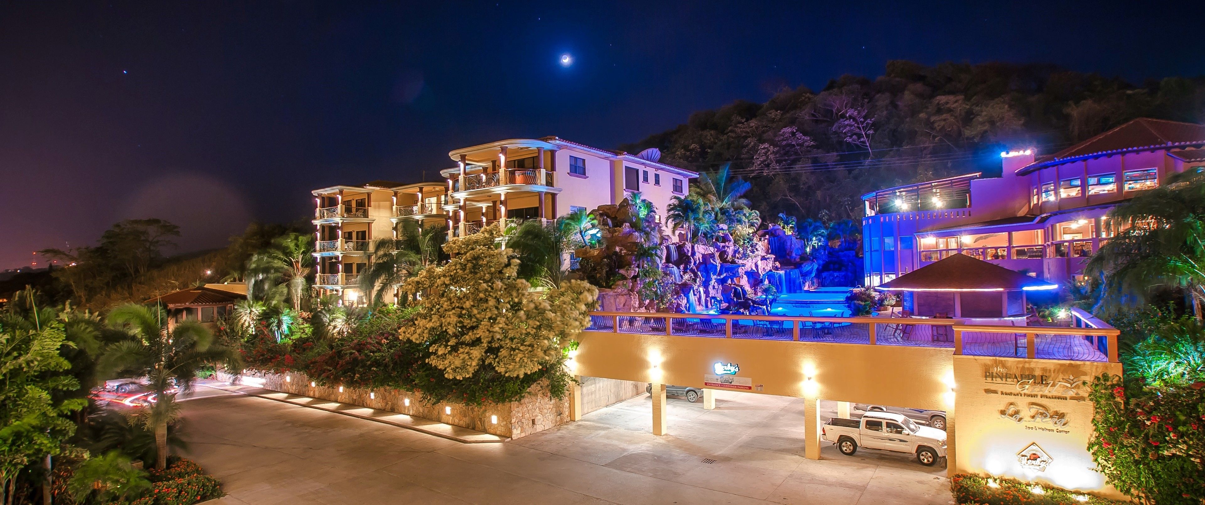 Un hotel de varios pisos con balcones, una cascada y un estacionamiento.