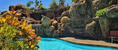 A pool with clear blue water, surrounded by rocky terrain and lush greenery.