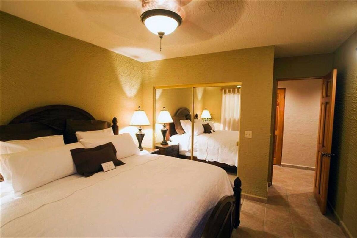 A hotel room with a large bed, bedside lamps, a mirror, and a ceiling fan.