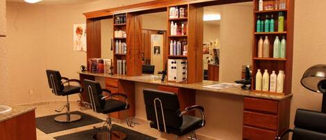 A salon with two black chairs, a mirror, and shelves with hair products.