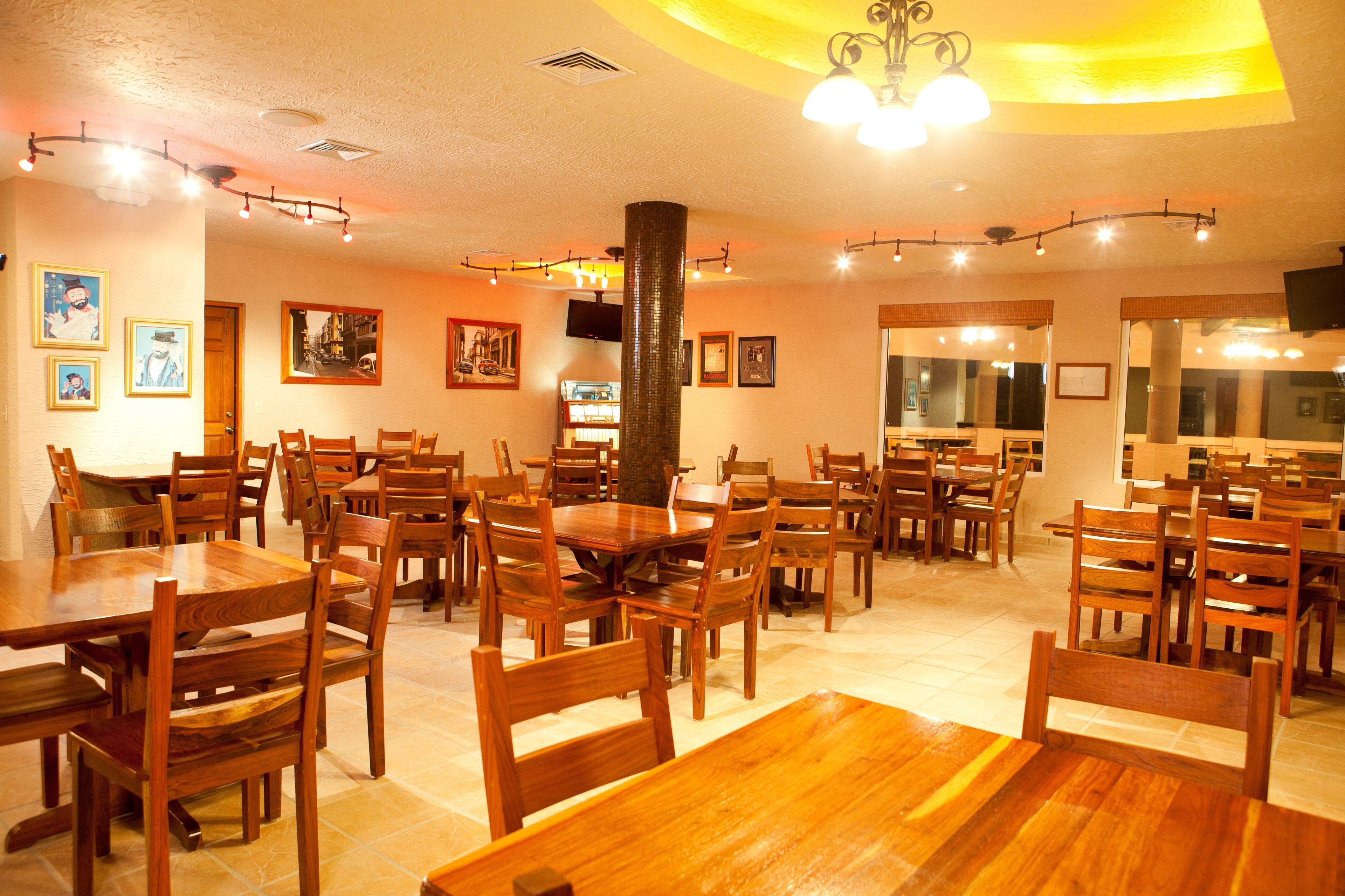 A restaurant with multiple wooden tables and chairs, a large pillar, and framed pictures on the walls.