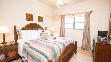 A bedroom with a wooden bed, two bedside tables with lamps, a television on a stand, and a window with curtains.