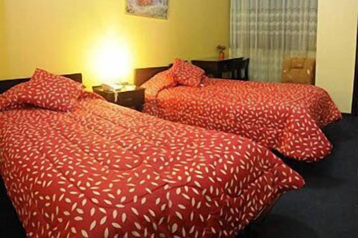Quarto de hotel com duas camas, uma mesa, uma cadeira e uma janela com cortinas.