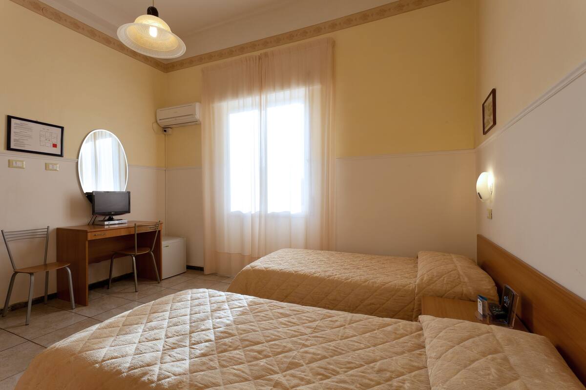 A hotel room with two beds, a desk with a computer, a chair, and a window with curtains.