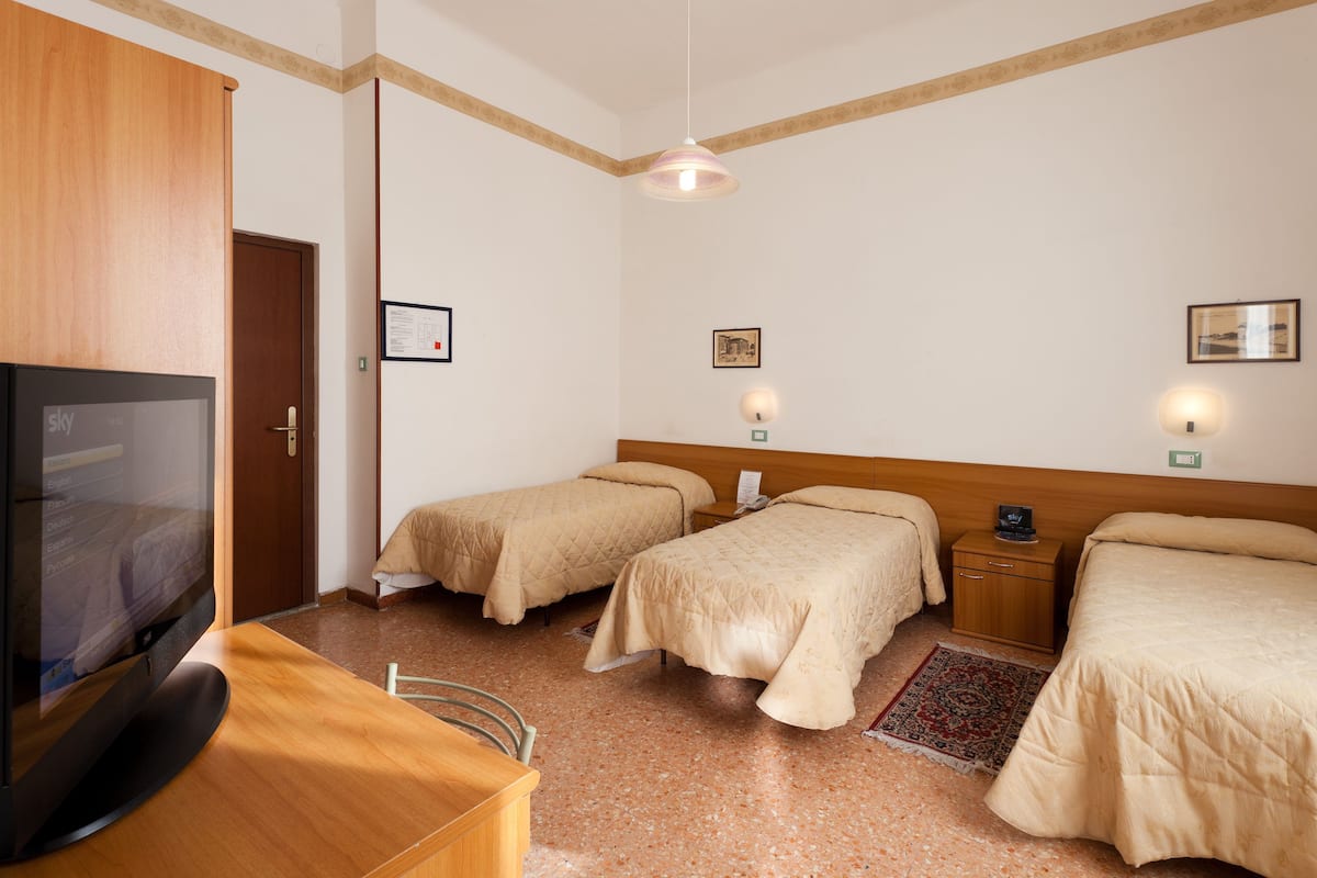 A hotel room with two beds, a wooden desk with a television, and a small rug.