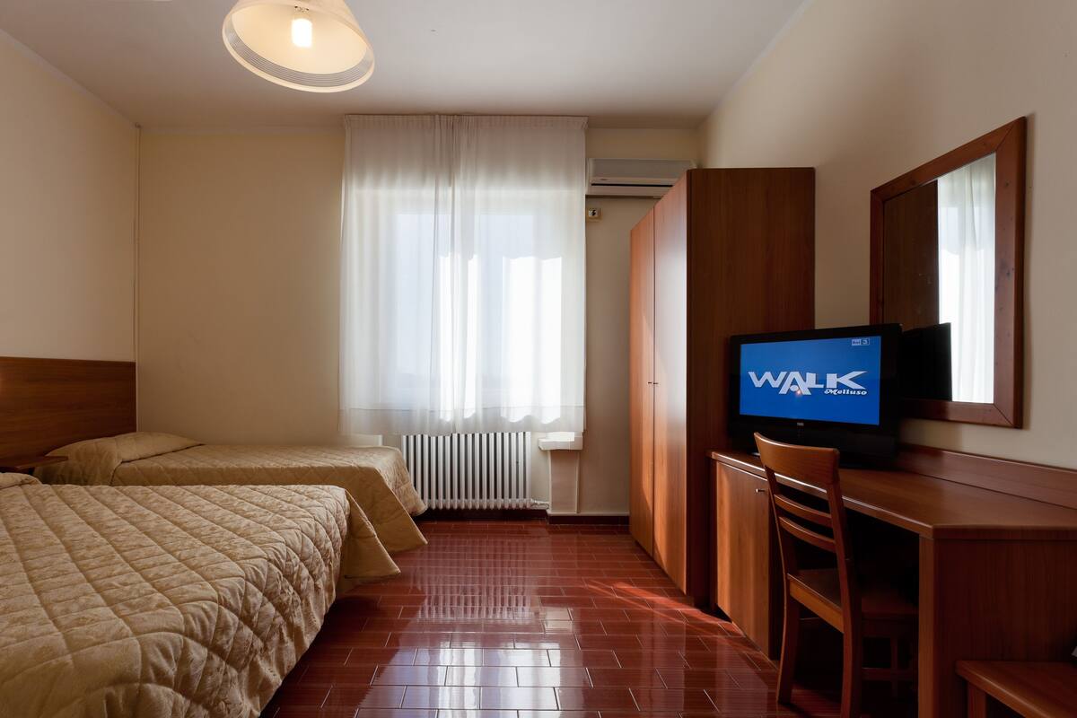 A hotel room with two beds, a TV, a wooden desk, and a chair.
