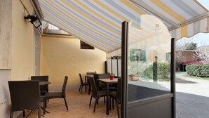 Un patio exterior con mobiliario de mimbre, una partición de vidrio y un toldo a rayas.