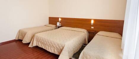 Habitación de hotel con dos camas individuales, cabeceros de madera, una mesita con un teléfono y una lámpara sobre las camas.