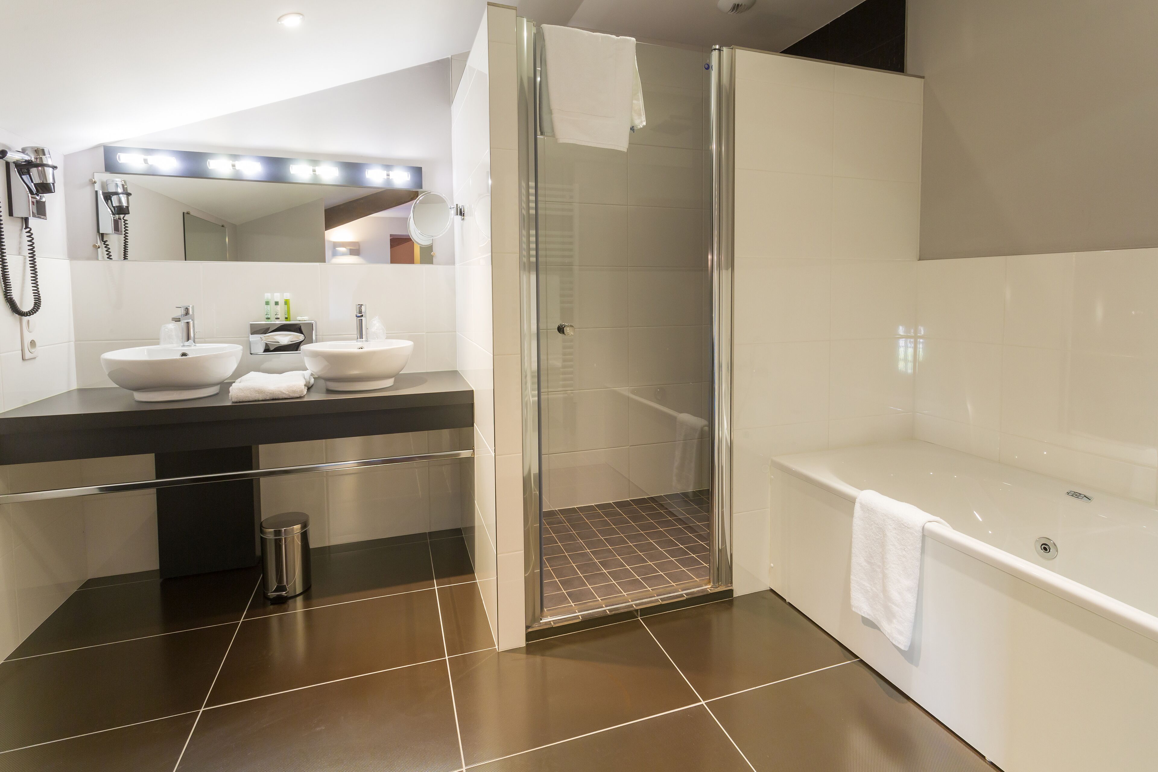 Un baño moderno con ducha de cristal, dos lavamanos y una bañera.