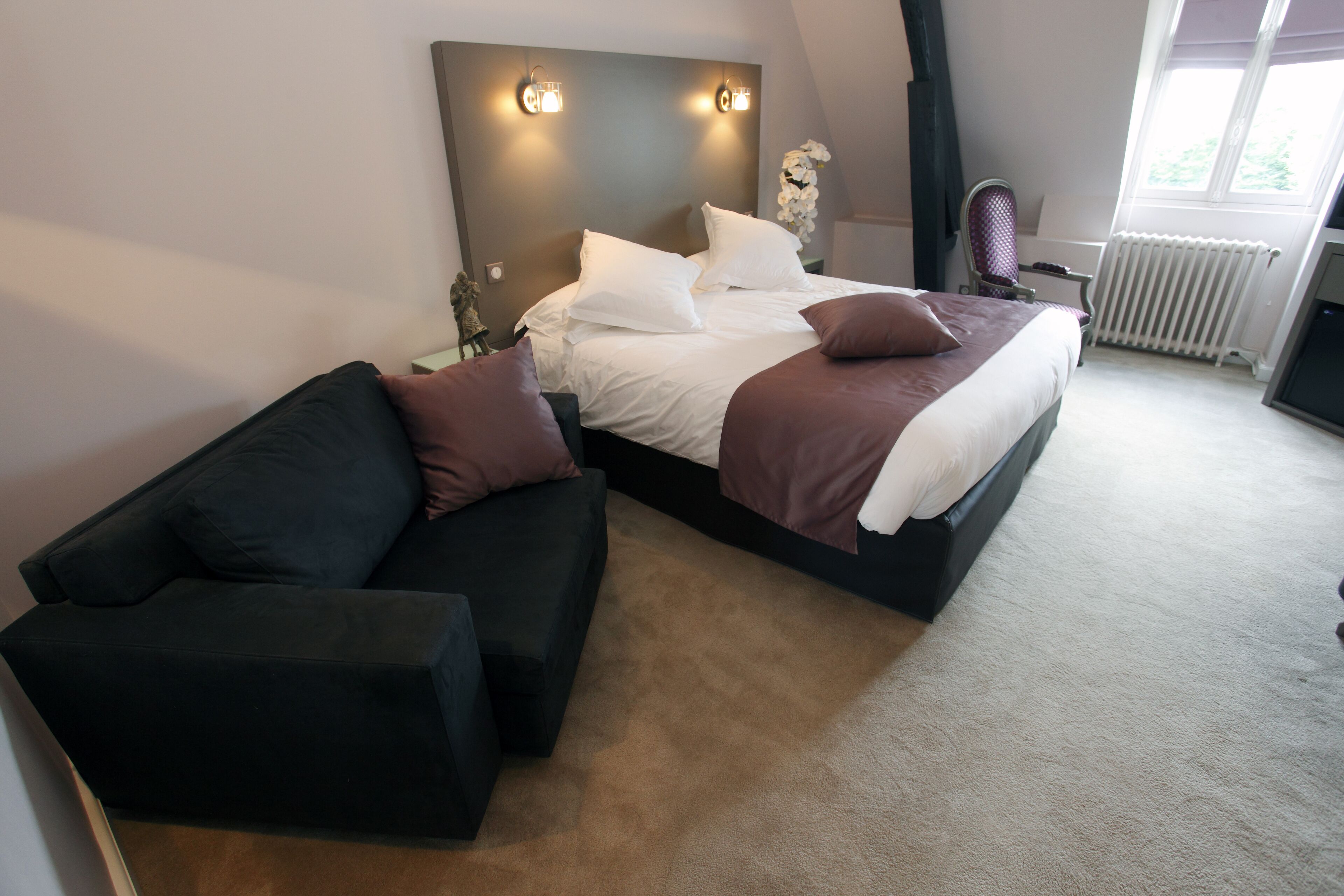 A bedroom with a bed, a black sofa, and a radiator.