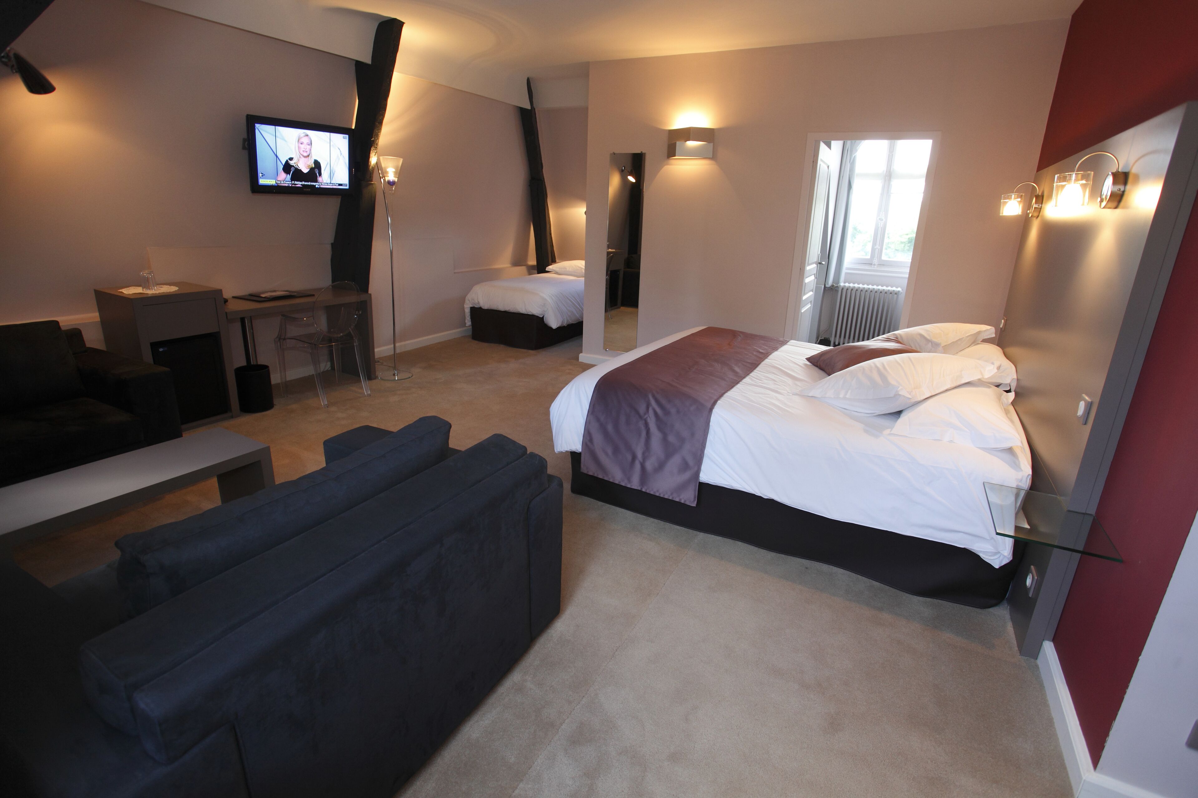 A modern hotel room with a large bed, a desk, a sofa, and a TV mounted on the wall.