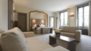 Quarto de hotel com cama, dois sofás, mesa de centro e janelas amplas.