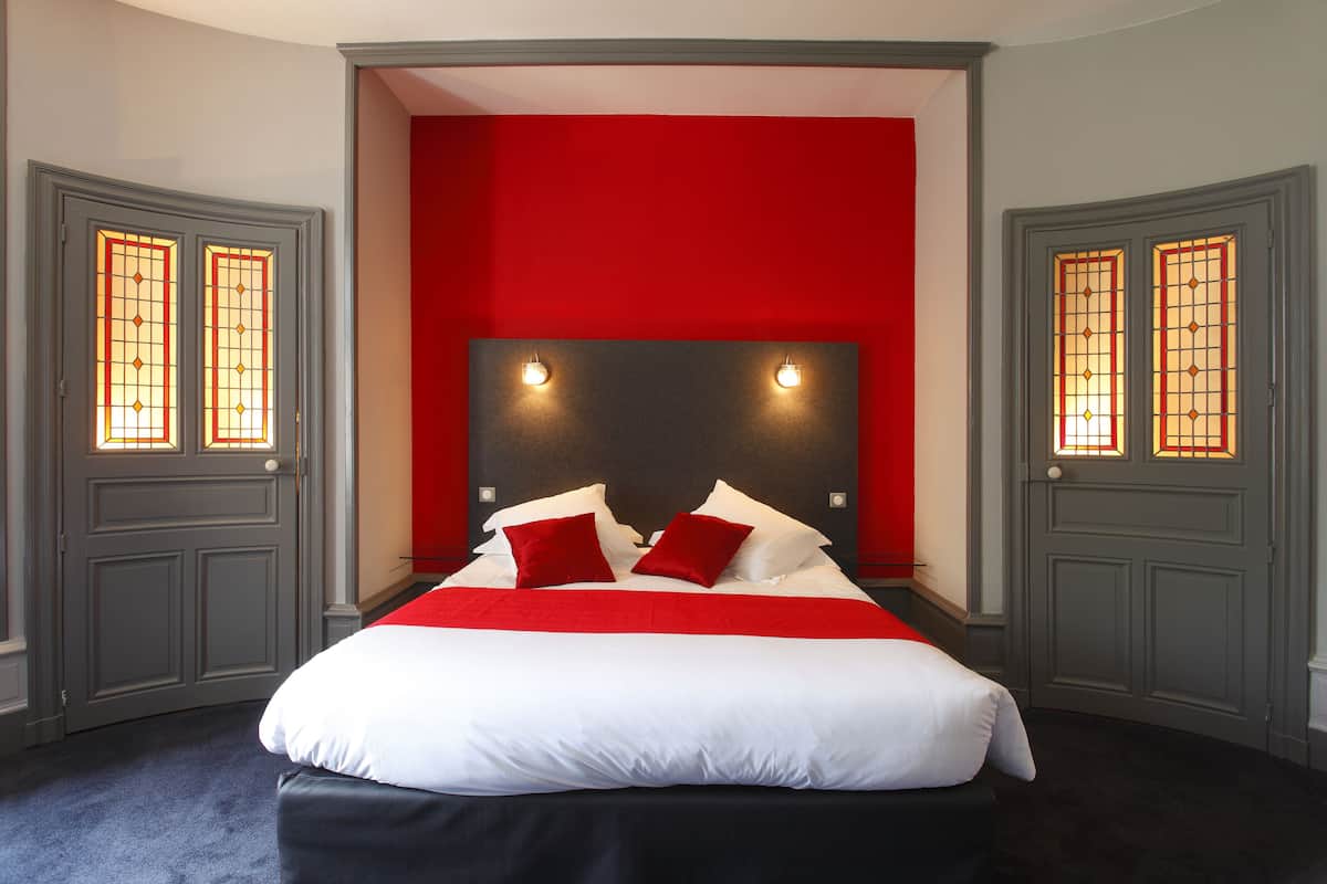 Ein Schlafzimmer mit einem großen Bett, roten Akzentwänden und zwei Türen mit Buntglasfenstern.