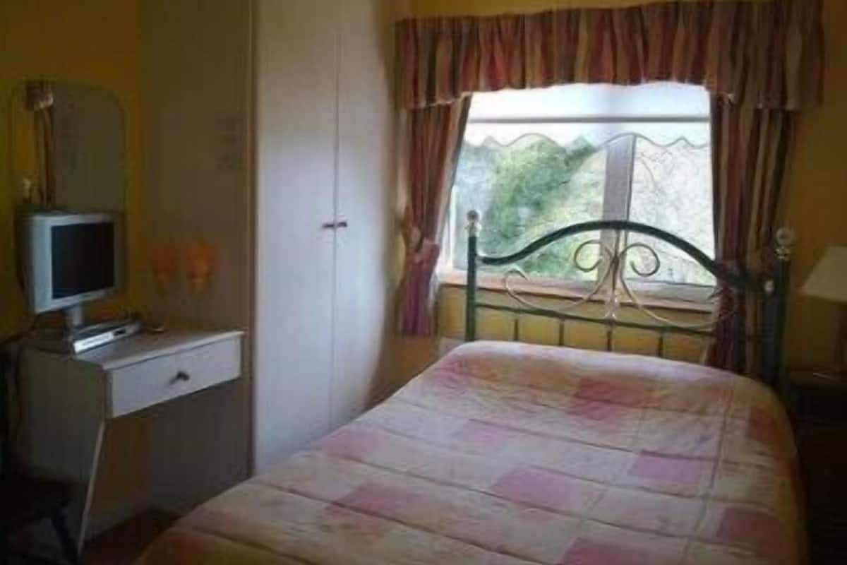 A bedroom with a bed, a dresser, a television, and a window with curtains.