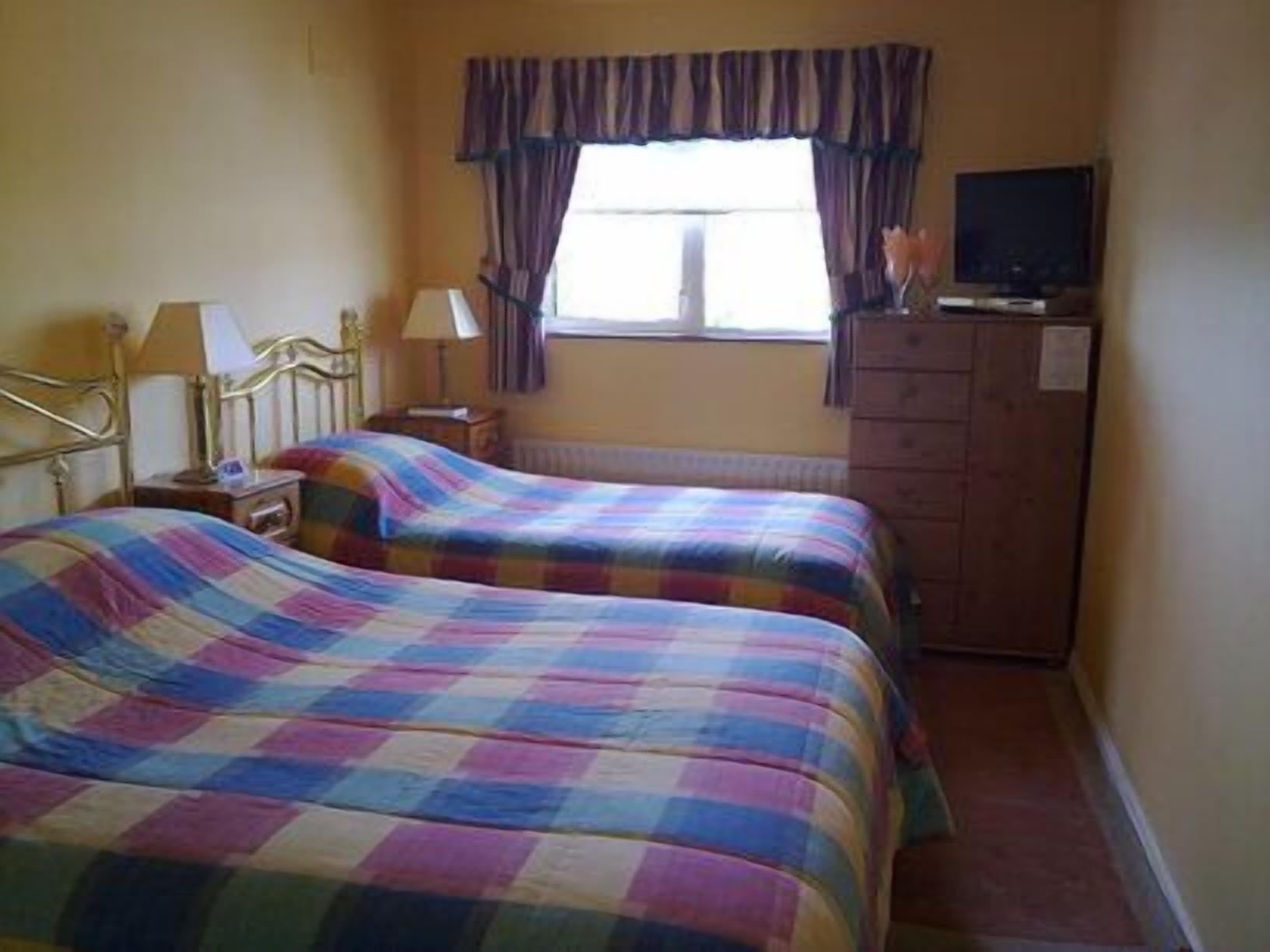 A room with two beds, a television, a dresser, and a window with curtains.