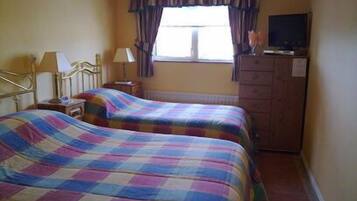 A room with two beds, a television, a dresser, and a window with curtains.