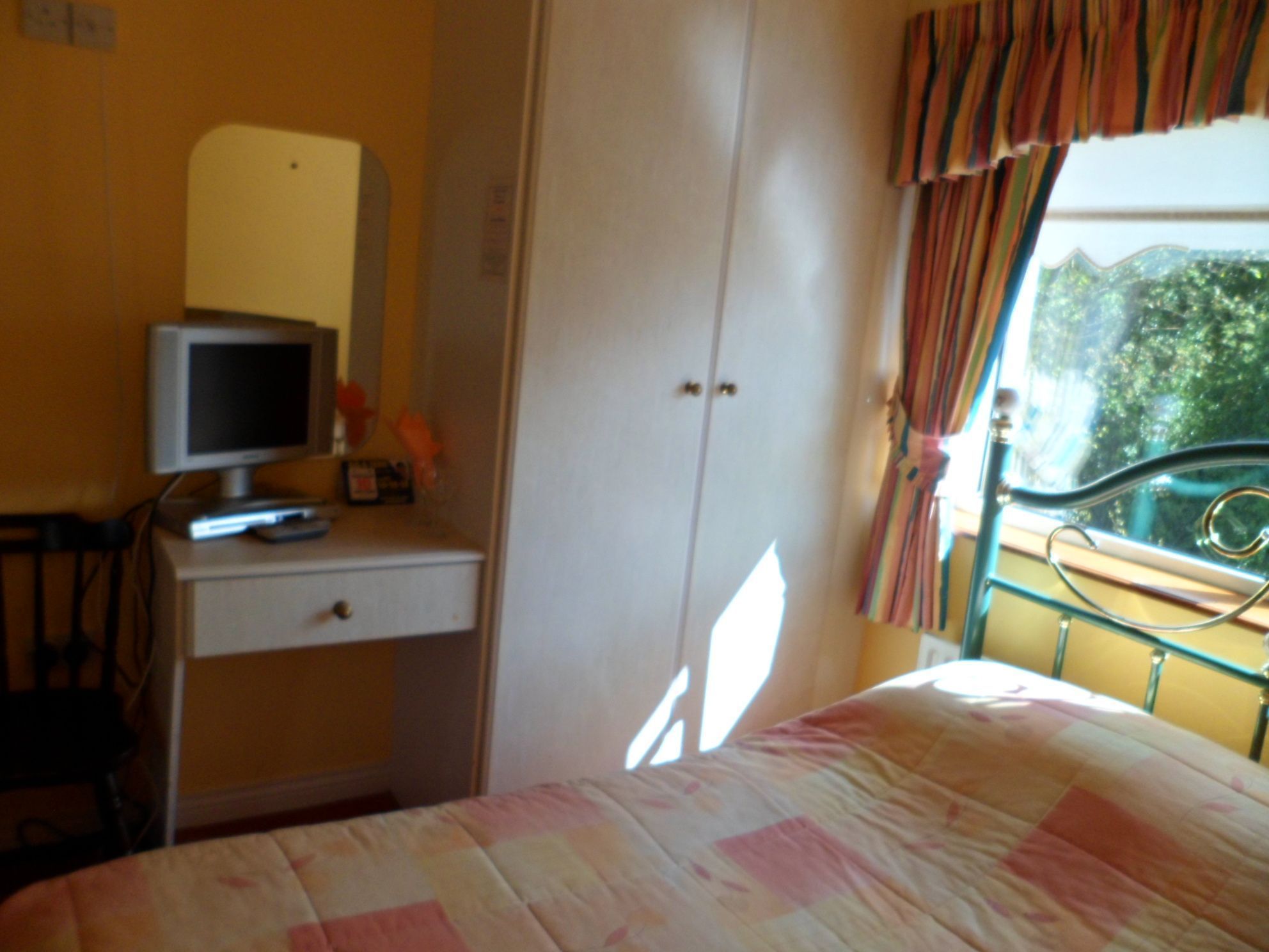 A bedroom with a bed, a desk with a computer, a wardrobe, and a window with curtains.