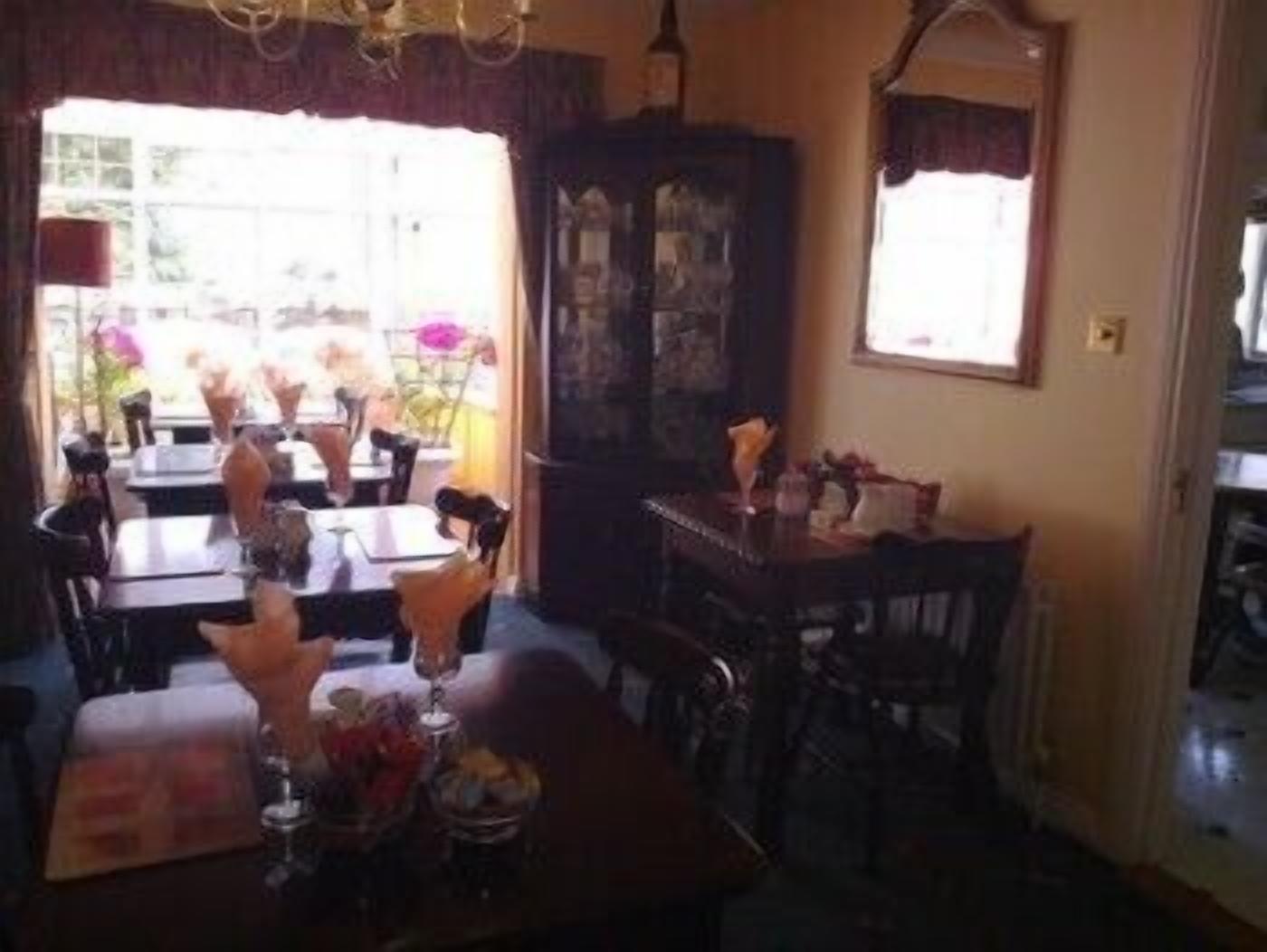 A dining area with tables and chairs, a chandelier, and a window with curtains.