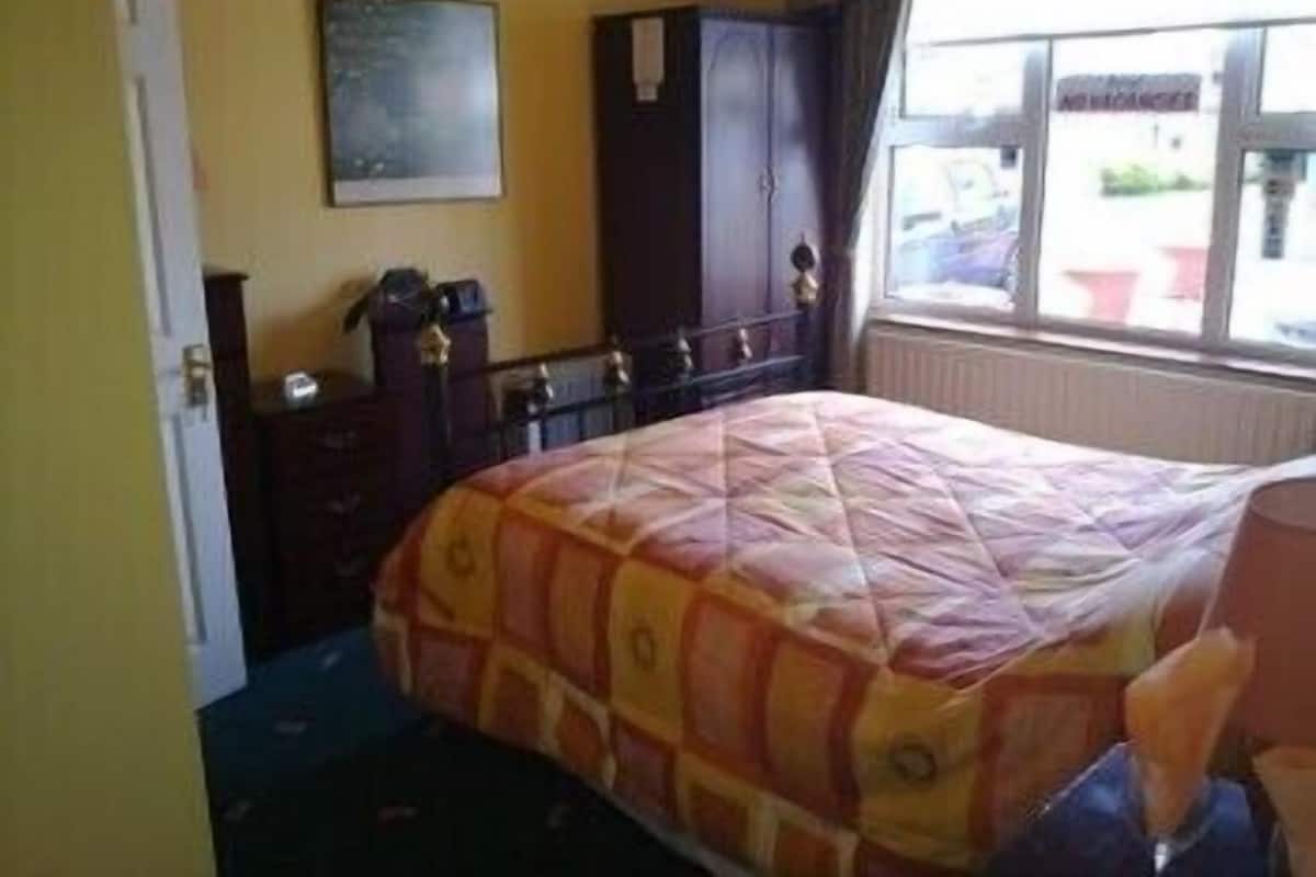 A bedroom with a bed, a dresser, a mirror, and a window with a view of the outside.