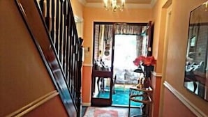 A narrow hallway with a wooden staircase on the left, a rug on the floor, and a door leading to a room with a blue carpet. - The Branches (Galway)