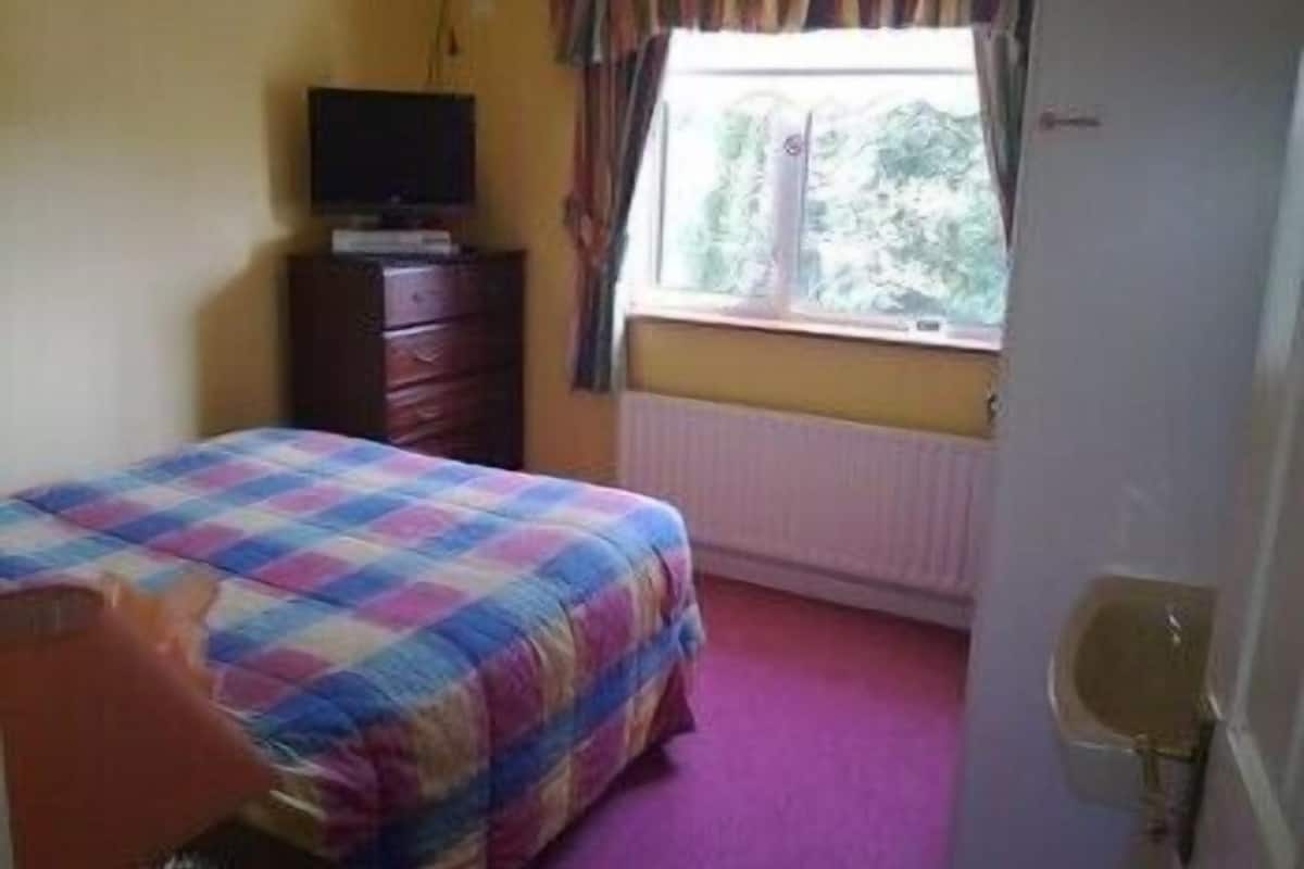 A bedroom with a bed, a dresser, a television, and a window with curtains.