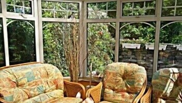 A conservatory with wicker furniture, a table with a vase, and a view of greenery outside. - The Branches (Galway)
