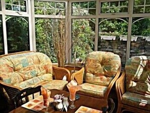 A conservatory with wicker furniture, a table with a vase, and a view of greenery outside. - The Branches (Galway)