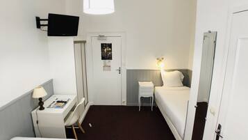 Hotelkamer met een bed, een bureau met stoel, een lamp, een aan de muur bevestigde televisie en een deur met een poster.