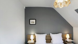 Un dormitorio moderno con techo inclinado, una cama con ropa de cama blanca, dos mesitas de noche con lámparas y un cuadro colgado en la pared.