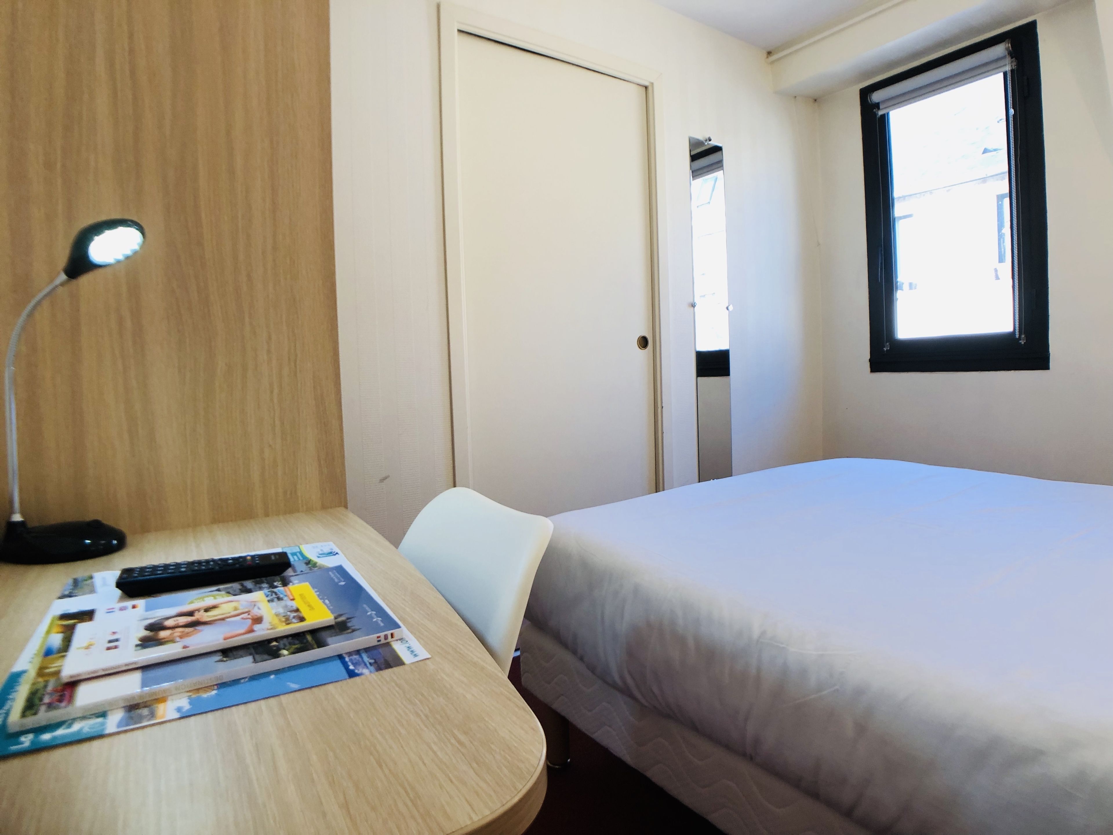 Una habitación de hotel con una cama, un escritorio con una lámpara, una silla y una ventana.