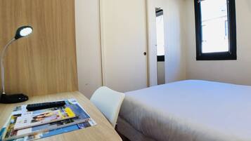 Una habitación de hotel con una cama, un escritorio con una lámpara, una silla y una ventana.