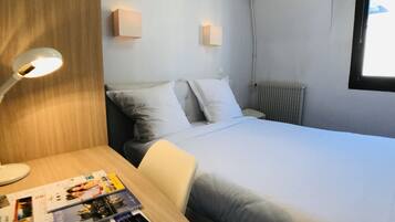 A hotel room with a bed, a desk with a lamp, and a window.
